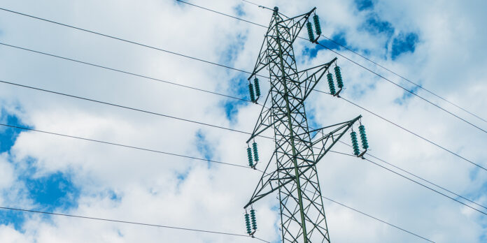 Spitze eines Strommastes vor blauem Wolkenhimmel