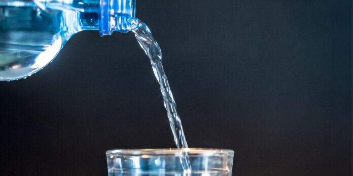 Eine Flasche schenkt ein Glas Wasser ein